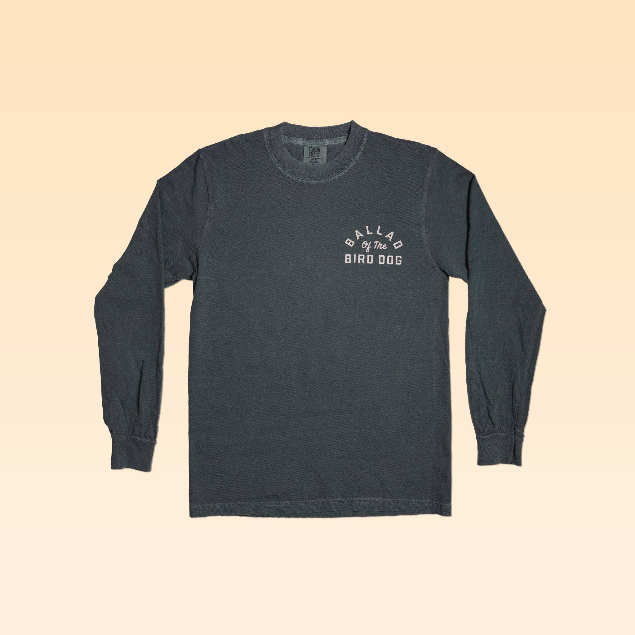 The Ballad of the Bird Dog Shop Shirt Long Sleeve | Rattlesnake Oval is a charcoal gray shirt with white print on the left chest, shown on a light beige background.