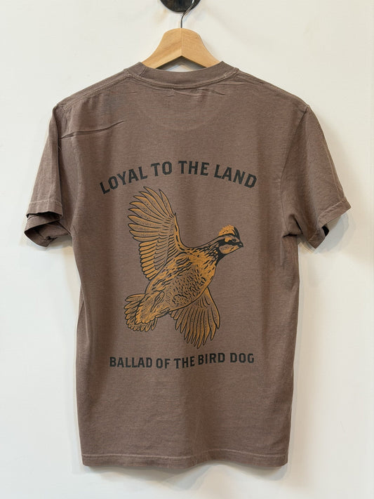 The Shop Shirt by Ballad of the Bird Dog features a brown design with a bird in flight illustration and "LOYAL TO THE LAND" and "BALLAD OF THE BIRD DOG" printed on the back.