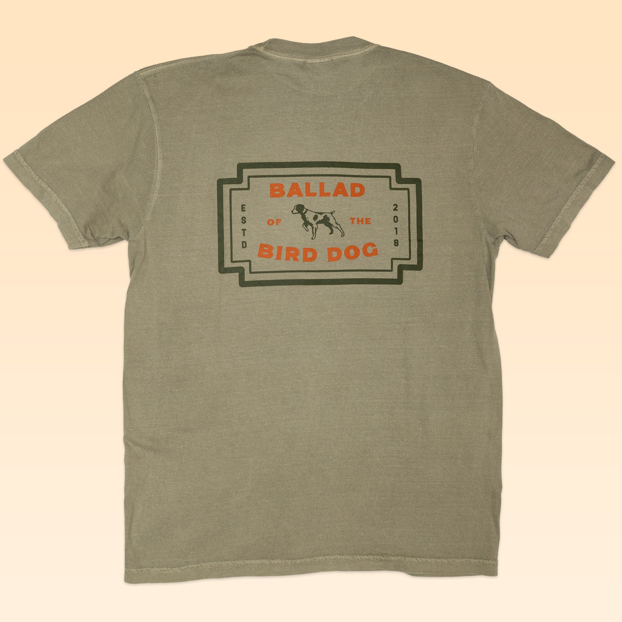 The Shop Shirt | Neon Revival by Ballad of the Bird Dog is a khaki tee with a back graphic featuring a dog and "Ballad of the Bird Dog ESTD 2016" in black, orange, and olive—ideal for fans of nostalgic or classic logo shirts.