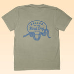 Back view of Ballad of the Bird Dog's Shop Shirt in khaki, featuring a blue "Ballad of the Bird Dog Texas" graphic and a rattlesnake oval logo—ideal for fans of unique, snake-themed apparel from the Desert Collection.