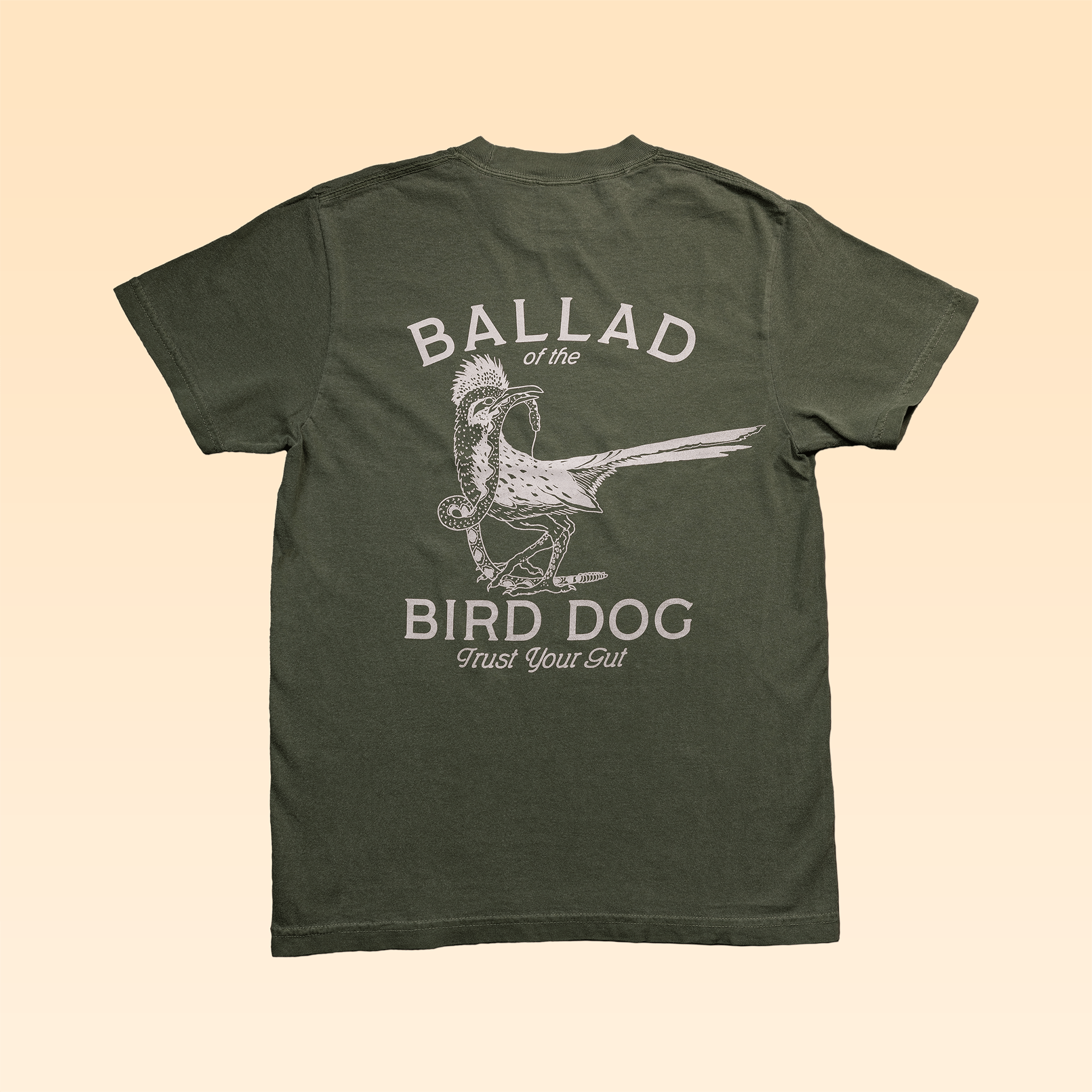 Olive green "Shop Shirt" by Ballad of the Bird Dog, featuring a large artist-style graphic of a roadrunner and rattlesnake with "Trust Your Gut" and "Ballad of the Bird Dog" text on the back.
