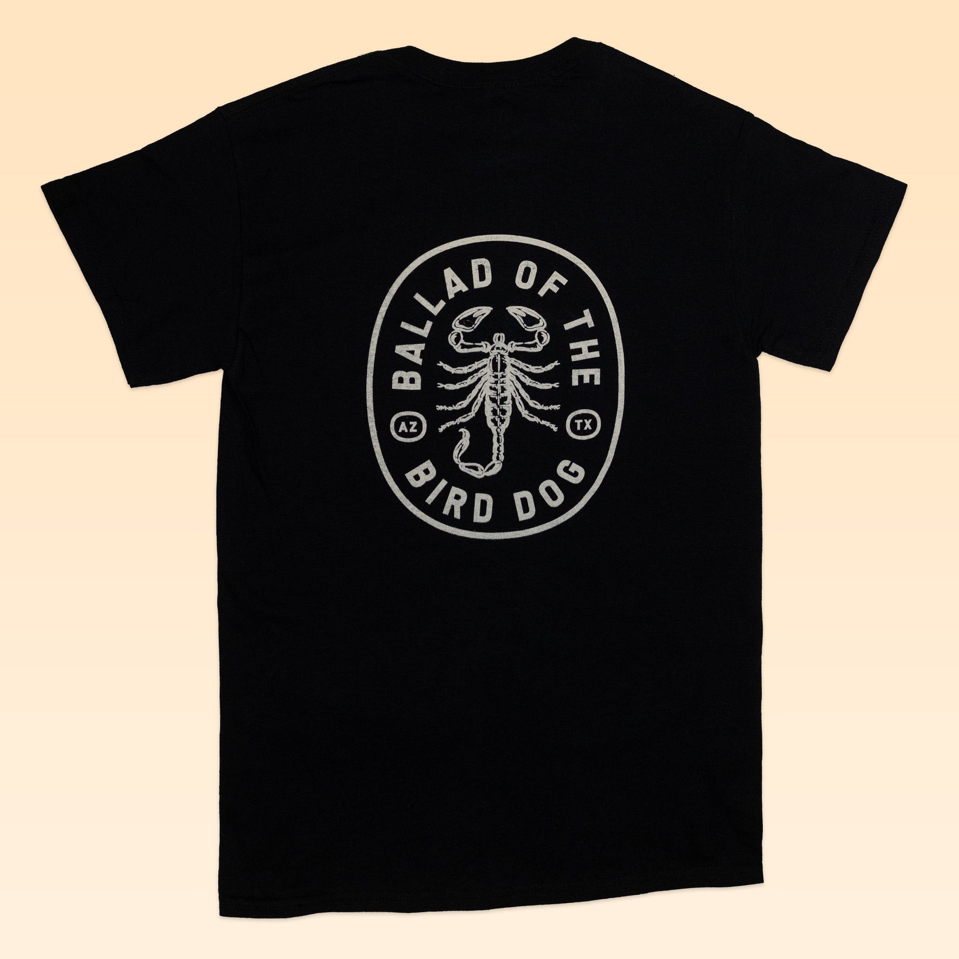 The Shop Shirt | Scorpion by Ballad of the Bird Dog features a black design with a white oval emblem and scorpion graphic on the back. Hand-printed and part of the Desert Scenes Collection, it blends bold style with artisanal detail.