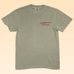 The Ballad of the Bird Dog Shop Shirt | Side By Side is a light olive green tee with a small red shotgun graphic and text on the left chest, displayed flat on a beige background.