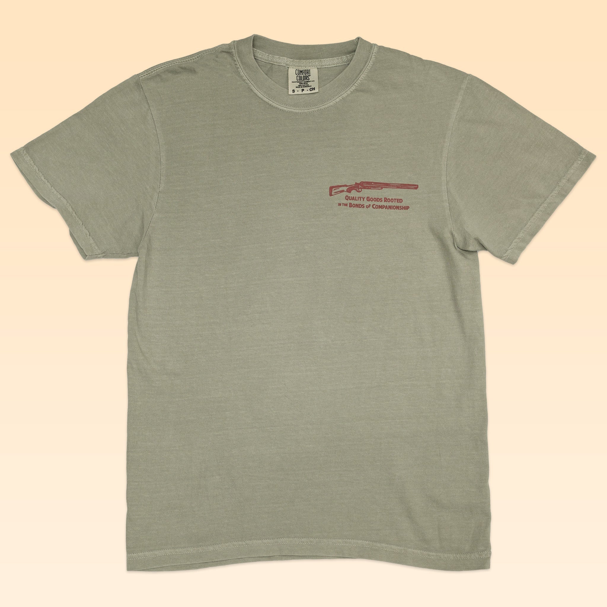 The Ballad of the Bird Dog Shop Shirt | Side By Side features light olive green short sleeves with a small red rifle graphic and text on the left chest—ideal for fans of quality goods and bird dog companionship.