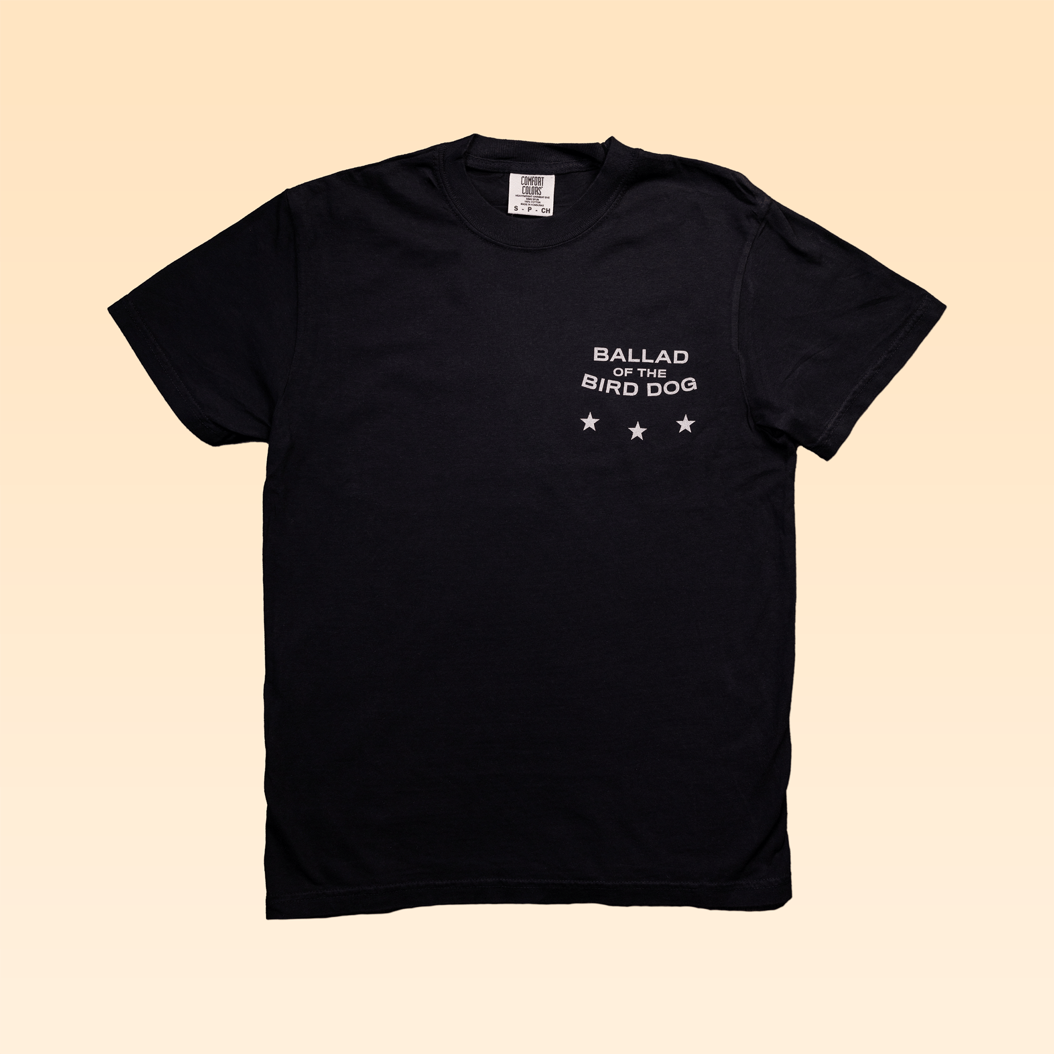Ballad of the Bird Dog Shop Shirt | Small Town Revival Glory: Black Comfort Colors tee with "BALLAD OF THE BIRD DOG" and three white stars on the left chest, shown against a light beige background.