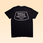 Back view of a black Shop Shirt from Ballad of the Bird Dog with "SMALL TOWN REVIVAL BRENHAM TEXAS" in white on a rounded rectangle—a classic Small Town Revival Glory tee celebrating community heritage.