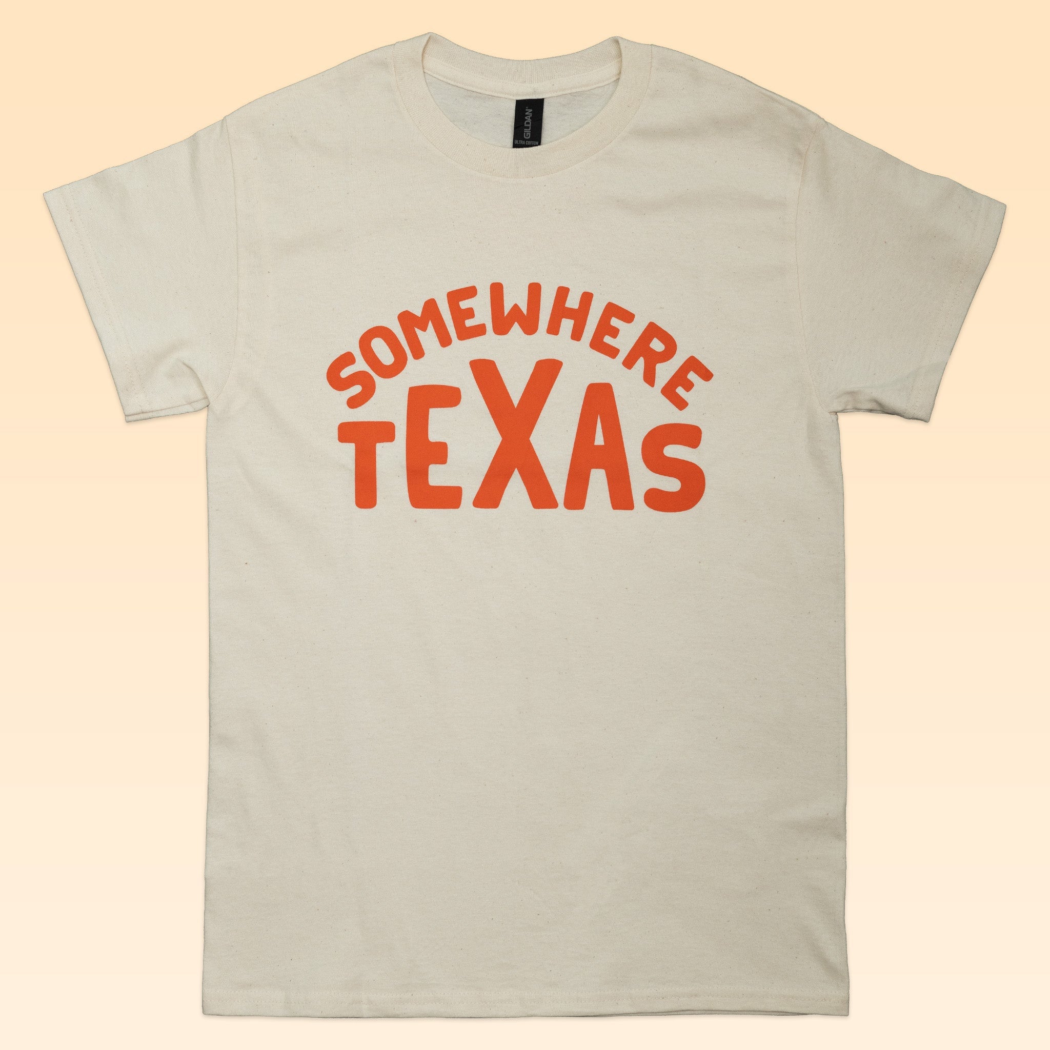 The Shop Shirt by Ballad of the Bird Dog features "SOMEWHERE TEXAS" in bold orange on cream—perfect for showcasing your Texas pride and small town style.