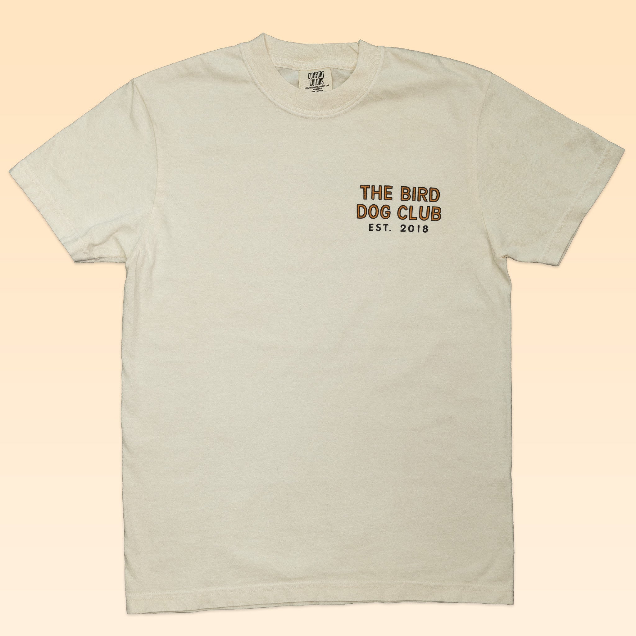 The Shop Shirt by Ballad of the Bird Dog features an off-white heritage outdoor style with "THE BIRD DOG CLUB EST. 2018" printed in small black and gold on the left chest—a subtle tribute to classic bird hunting shirts.