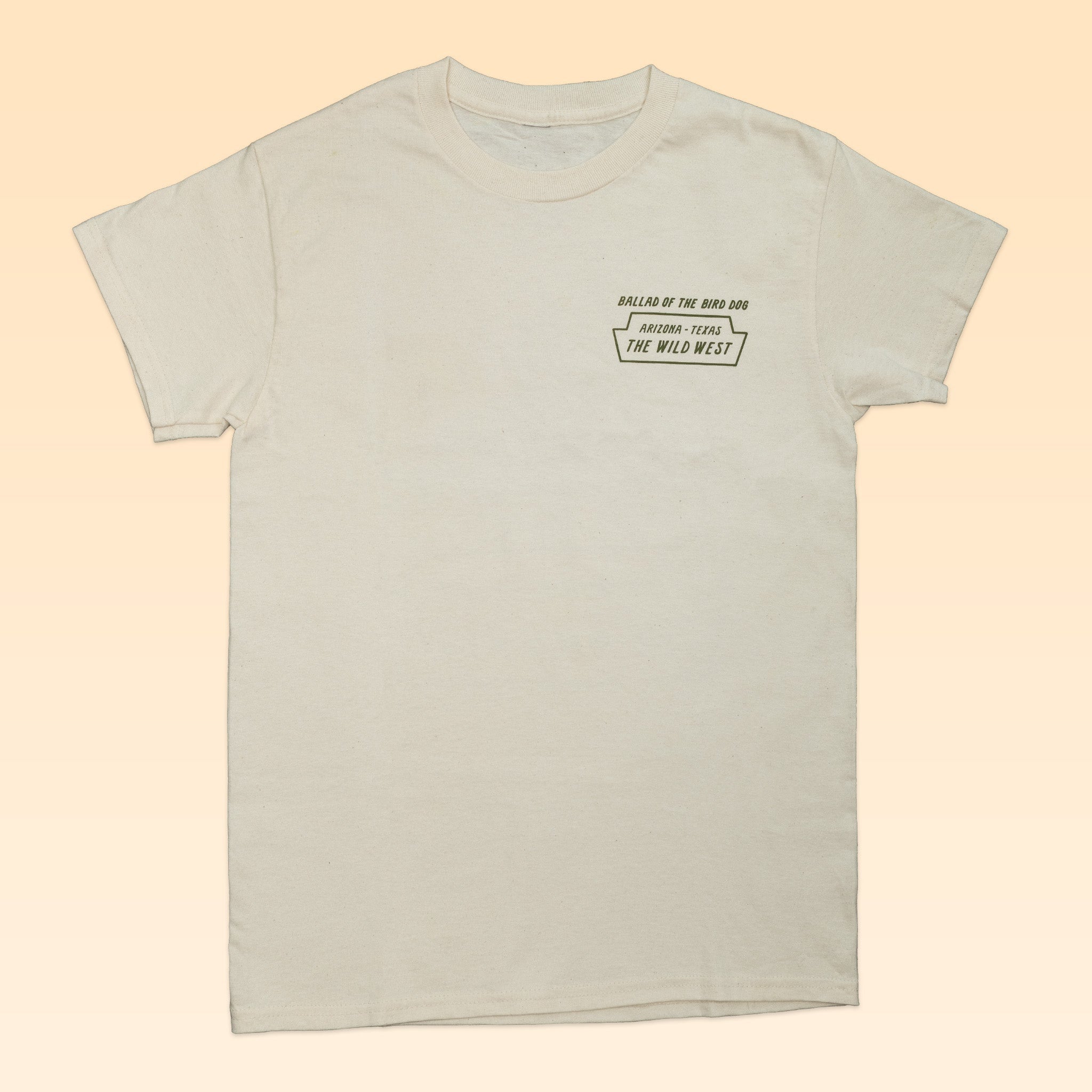 The Ballad of the Bird Dog "Shop Shirt | The Wild West" features an off-white desert hue with small black text, "Rallies of the Mad Dog" and "The Wild West," on the left chest. Shirt shown laid flat on a light beige background.