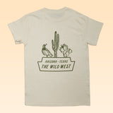 The Shop Shirt | The Wild West by Ballad of the Bird Dog is a beige tee with a green bird, cacti, and "ARIZONA - TEXAS THE WILD WEST" graphic on the back—perfect for desert wildlife fans.