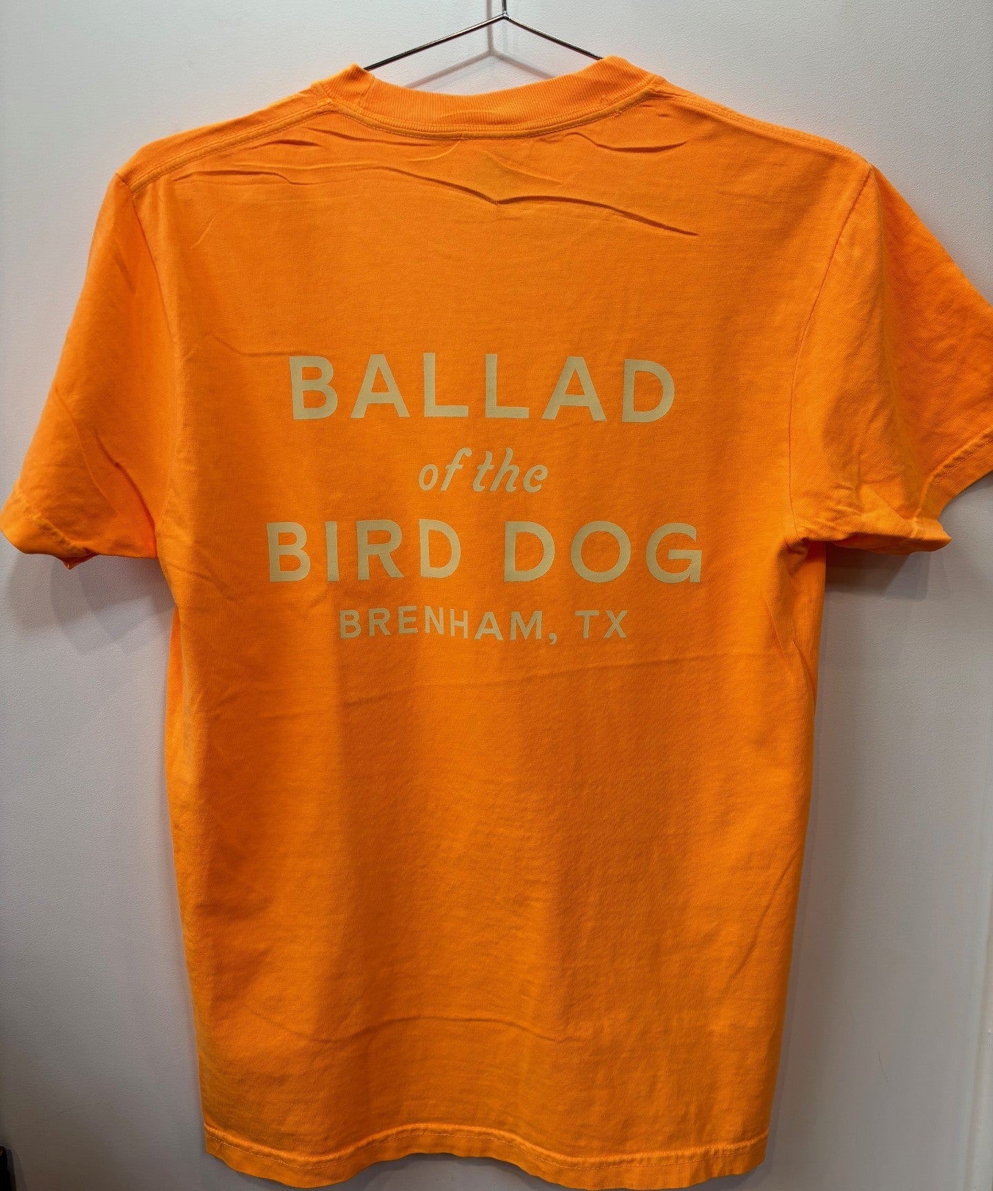 The Ballad of the Bird Dog Shop Shirt | Upland is an orange T-shirt with "BALLAD of the BIRD DOG BRENHAM, TX" printed in white on the back.
