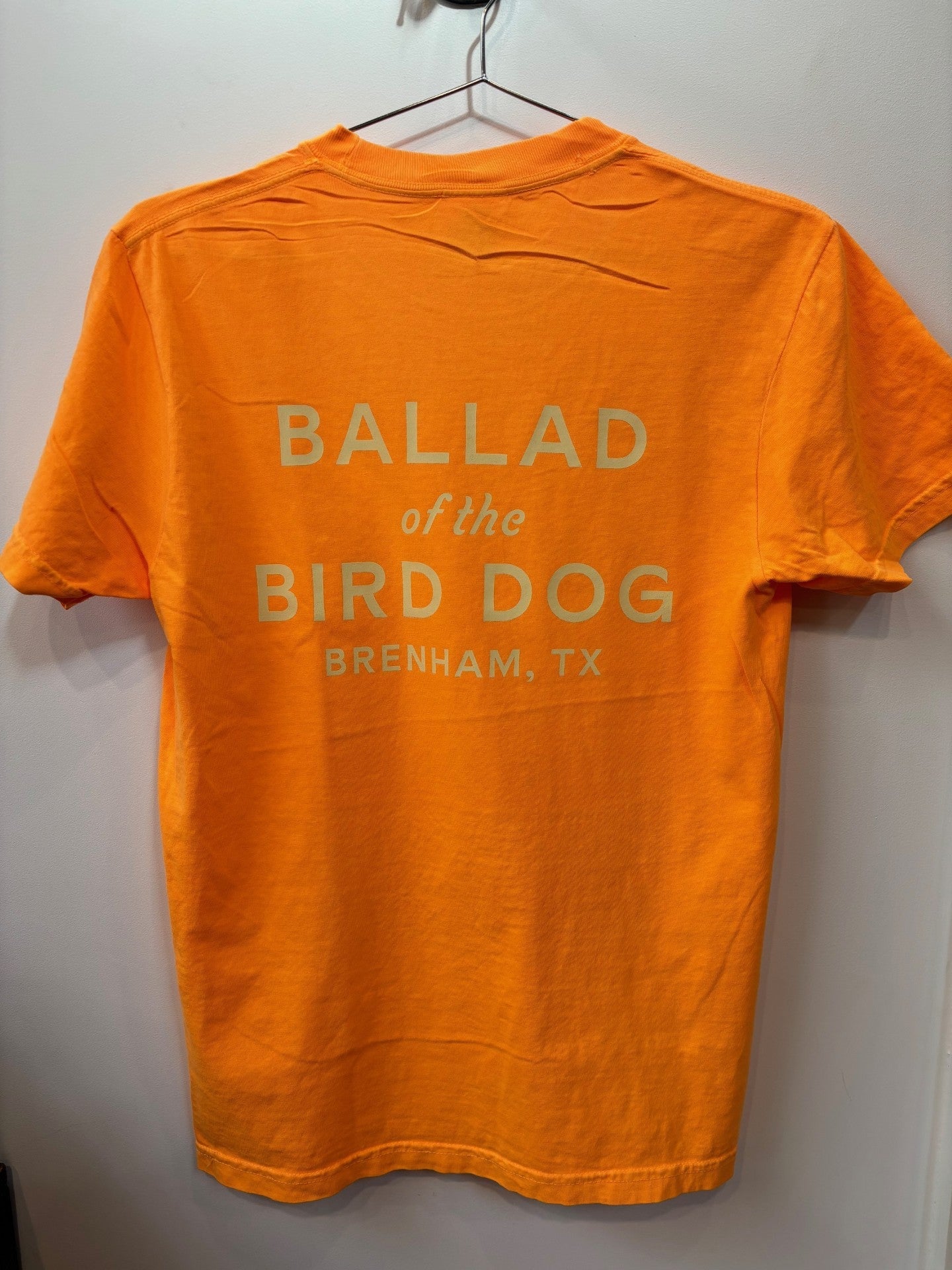 The Ballad of the Bird Dog Shop Shirt | Upland is an orange T-shirt with "BALLAD of the BIRD DOG BRENHAM, TX" printed in white on the back.