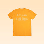 The Ballad of the Bird Dog "Shop Shirt | Upland" is a yellow tee with “BALLAD of the BIRD DOG BRENHAM, TX” in white on the back, shown on a light peach background.