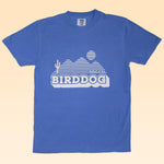 The Shop Shirt by Ballad of the Bird Dog features a blue vintage design with white mountain, cactus, and hot air balloon graphics plus "Ballad of the Bird Dog" text—a unique pick for style lovers.