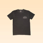 The Shop Shirt by 1844 Liquor Market is a plain dark gray tee with a small white rectangular "Winner Winner Chicken Dinner" logo on the left chest, displayed on a light beige background.