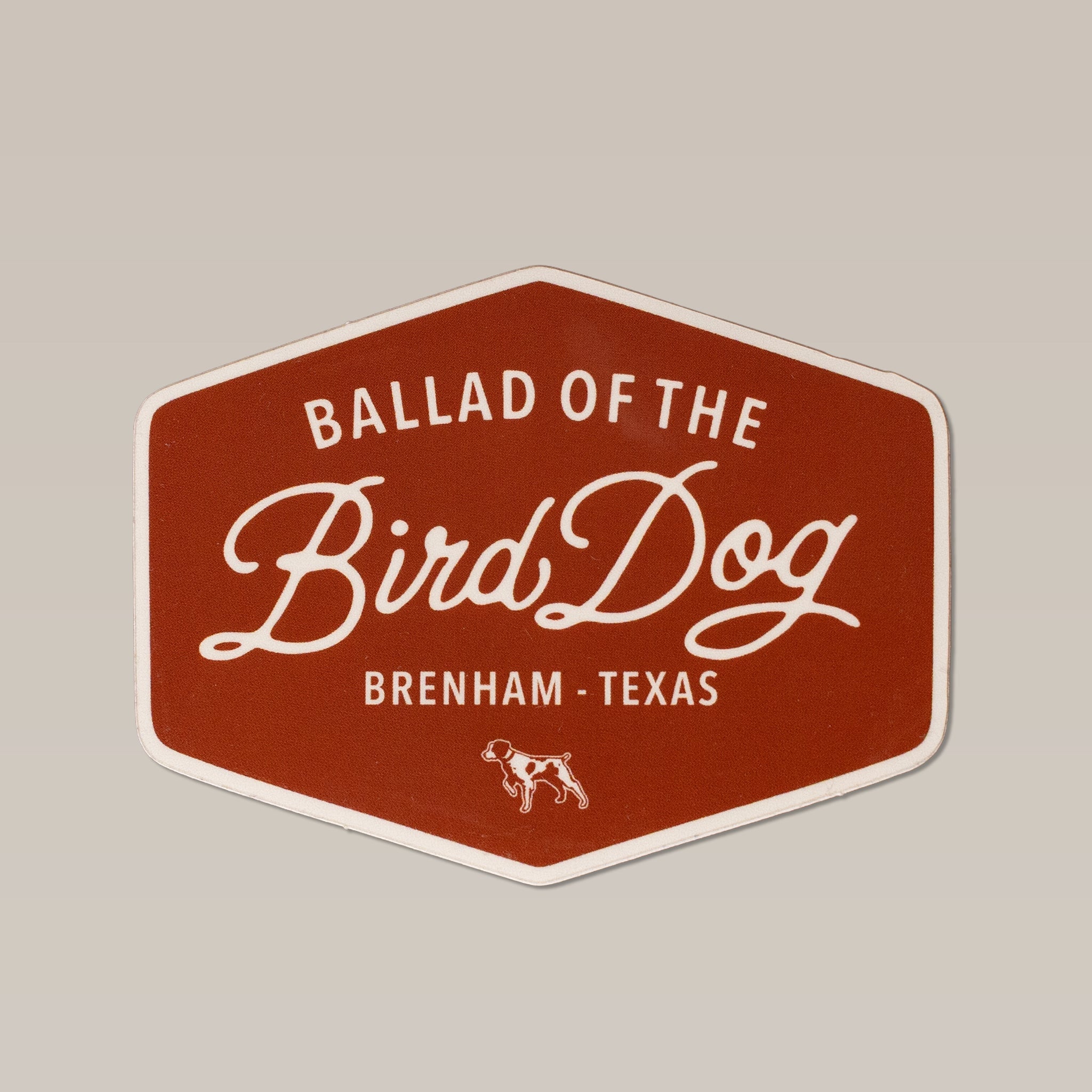 The Ballad of the Bird Dog Shop Sticker features a hexagonal Bird Dog Badge design with "Ballad of the Bird Dog, Brenham, Texas" in white script on brown, and a small dog illustration—a vintage-inspired nod to hunting heritage.