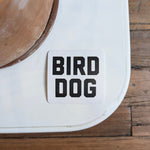 The Shop Sticker | Bird Dog Honor by Ballad of the Bird Dog features "BIRD DOG" in bold black letters on a white square—ideal for hunting and outdoor adventure enthusiasts.