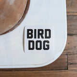The Shop Sticker | Bird Dog Honor by Ballad of the Bird Dog features "BIRD DOG" in bold black letters on a white square—ideal for hunting and outdoor adventure enthusiasts.