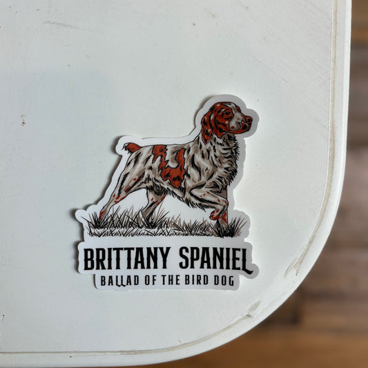 A Shop Sticker from Ballad of the Bird Dog features an illustrated Brittany Spaniel with “BRITTANY SPANIEL” and “BALLAD OF THE BIRD DOG” printed below the image on a white surface.