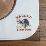 The Shop Sticker | Retriever by Ballad of the Bird Dog features a dog watching birds with "Ballad of the Bird Dog" in red and black on a white background over wooden floorboards.