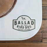 A white surface displays the Ballad of the Bird Dog "Heritage Lives Here" Shop Sticker with a dog silhouette; part of a wooden floor is visible.