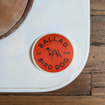 A round, durable Upland Orange Bird Dog Shop Sticker by Ballad of the Bird Dog features a central dog illustration against a white background—ideal for coolers and outdoor adventures.