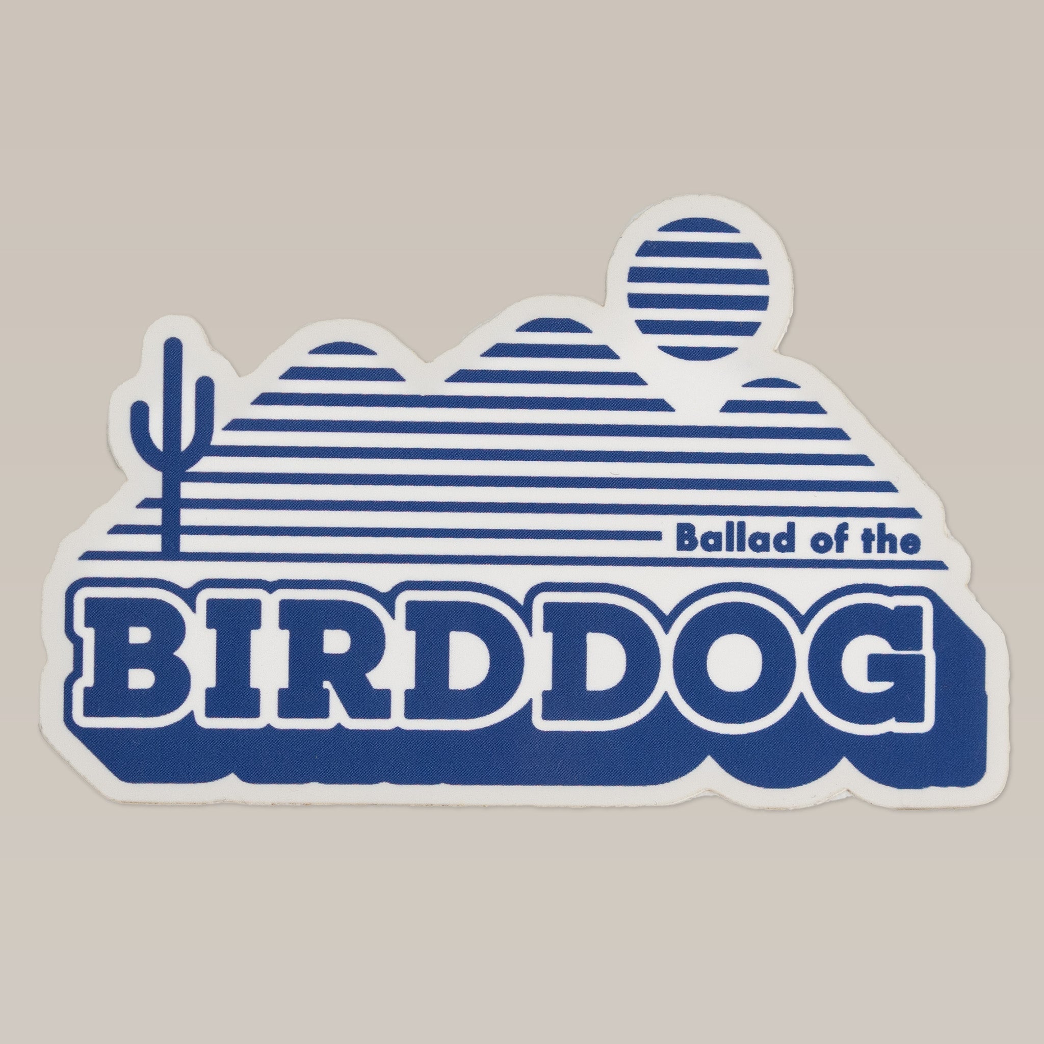 The Shop Sticker | Vintage Bird Dog by Ballad of the Bird Dog features bold "Ballad of the BIRDDOG" text, blue stylized mountains, a sun, and a cactus—capturing vintage desert vibes from their signature series.