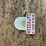 A Shop Sticker from Mescalito Coffee features a gold sunburst on wood with bold red "Mescalito Coffee" text, reflecting the brand's small-town coffee shop vibe.