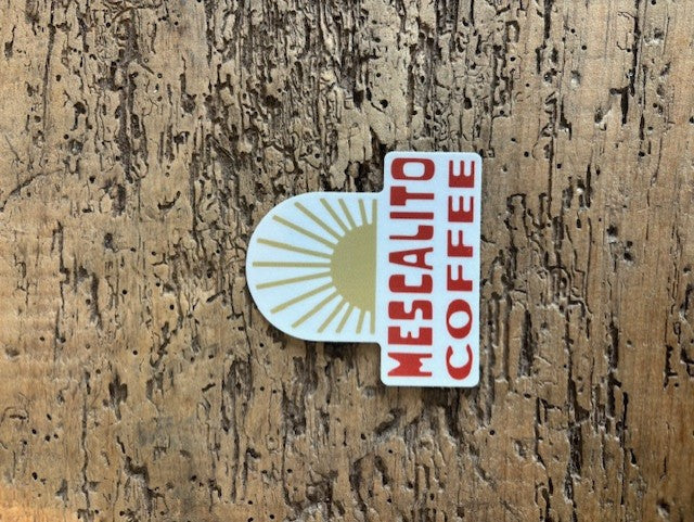 A Shop Sticker from Mescalito Coffee features a gold sunburst on wood with bold red "Mescalito Coffee" text, reflecting the brand's small-town coffee shop vibe.