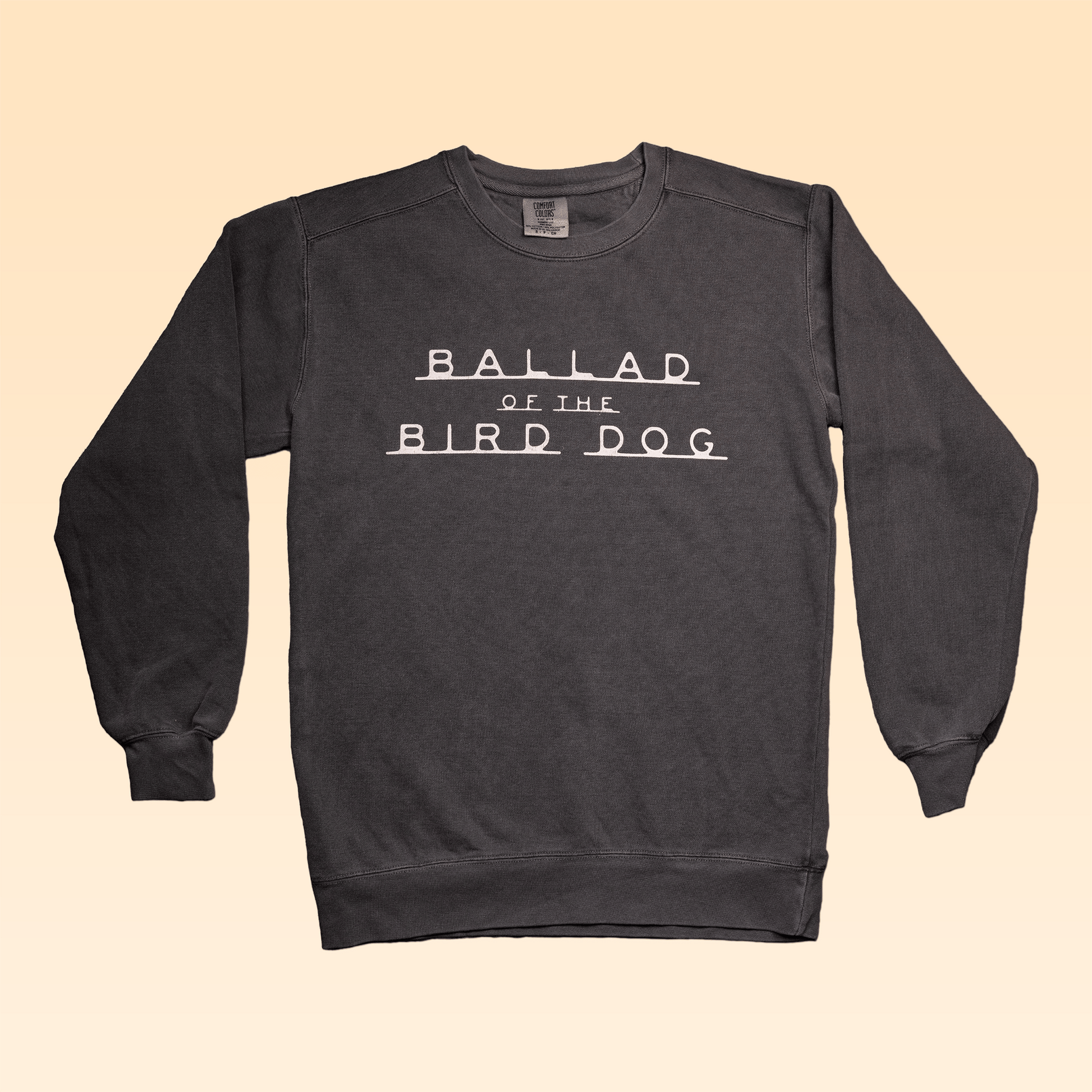 The Ballad of the Bird Dog Terlingua charcoal Comfort Colors crewneck sweater features "BALLAD OF THE BIRD DOG" in white, shown on a beige gradient background.