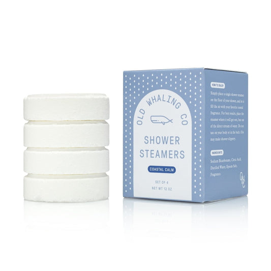 Four white shower steamers are stacked beside a blue box labeled "Shower Steamers | Coastal Calm | Old Whaling Co" by Old Whaling Co., offering a spa-like shower experience. The box features ingredients and directions.