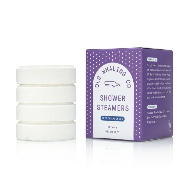 Four white handmade shower steamers sit next to a purple Old Whaling Co. box labeled "Shower Steamers | French Lavender," creating a spa-like shower experience.