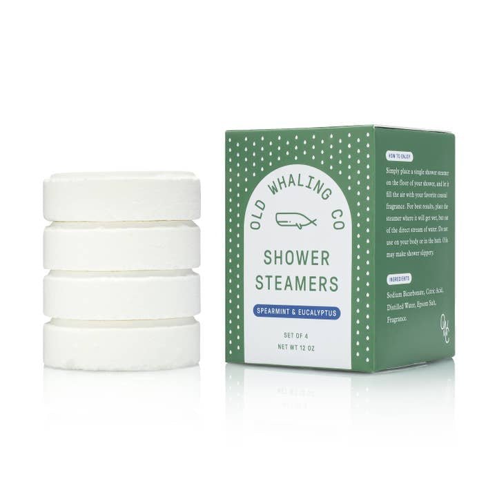 A stack of four white handmade Shower Steamers by Old Whaling Co. sits beside a green and white box labeled "Spearmint + Eucalyptus," perfect for creating a spa-like shower experience.