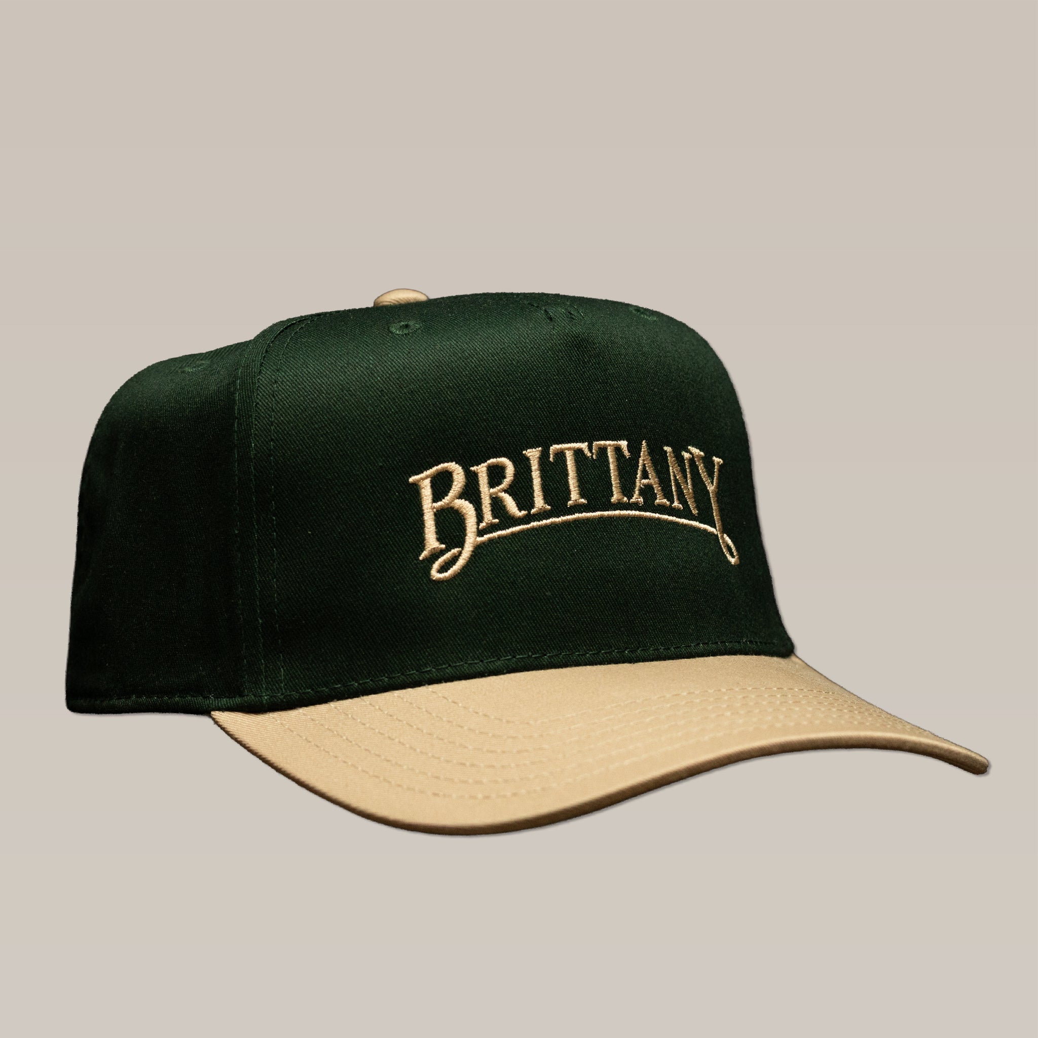 Dark green Bird Dog Series Hat | Brittany featuring a tan brim and “BRITTANY” embroidered in tan thread.