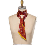 A mannequin showcases the Jenni Earle Silk Twilly Scarf, “Giddy Up,” featuring yellow and pink horseshoe and stirrup designs, loosely tied for a vintage western flair.