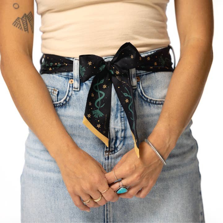 A person in light blue jeans and a beige top styles the Jenni Earle “Saddle Up and Lasso the Star” Silk Twilly Scarf as a belt, accessorized with rings and a bracelet.