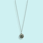 The Silver Compass Necklace by Ornamental Things features a round, marble-like stone and a functional compass, shown against a light blue background.