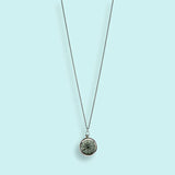 The Silver Compass Necklace by Ornamental Things features a round, marble-like stone and a functional compass, shown against a light blue background.