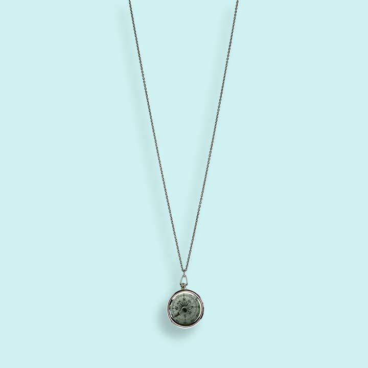 The Silver Compass Necklace by Ornamental Things features a round, marble-like stone and a functional compass, shown against a light blue background.