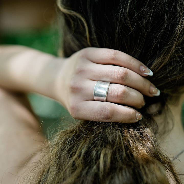 A person with long brown hair holds their hair, showcasing the Silver Concave Ring by Ornamental Things on their finger and nails featuring a white tip design.