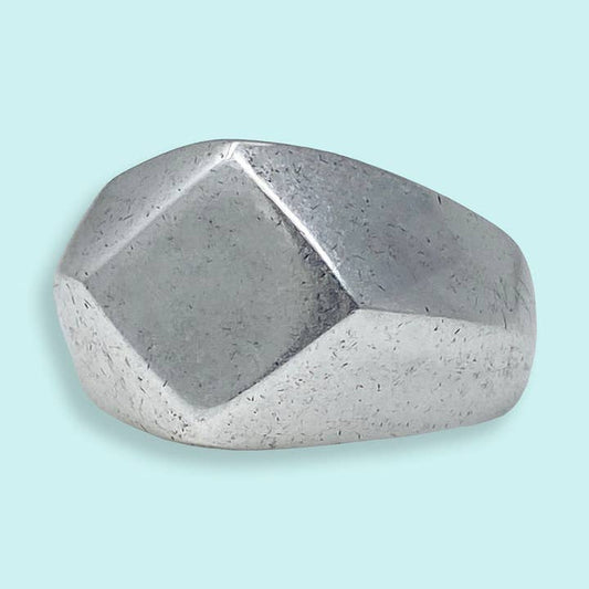 The Silver Facet Ring by Ornamental Things features a chunky, geometric design with a faceted silver surface, displayed on a light blue background.
