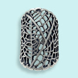 The Silver Leaf Lace Ring by Ornamental Things is a wide sterling silver ring featuring an intricate openwork lace pattern, shown on a light blue background.