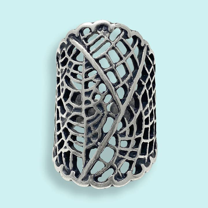 The Silver Leaf Lace Ring by Ornamental Things features an intricate dried leaf pattern with scalloped edges in sterling silver on a light blue background.
