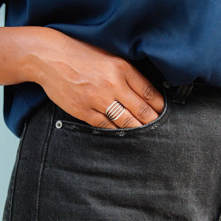A person wears the Silver Line Ring by Ornamental Things, resting their hand on the pocket of dark jeans and sporting a tucked-in navy shirt.