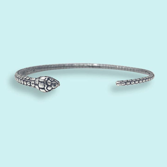 The Silver Open Snake Bangle Bracelet by Ornamental Things features a silver-plated serpent design with a head at one end and a tail at the other, shown against a light blue background.