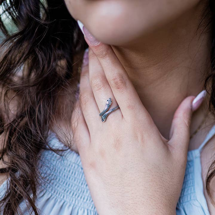 A person with long, wavy hair touches their neck, showing off the elegant Silver Snake Ring by Ornamental Things on their finger.