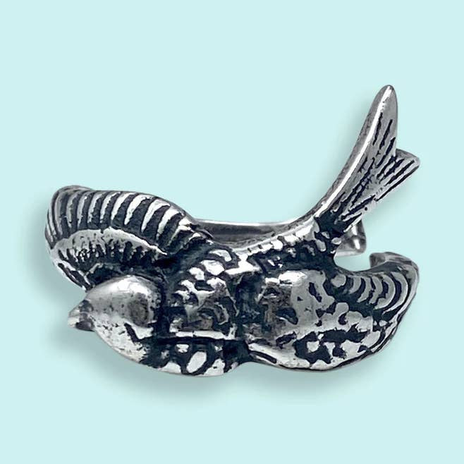 The Silver Sparrow Bird Ring by Ornamental Things is an adjustable silver ring shaped like a bird in flight, with detailed feather engravings, shown on a light blue background.