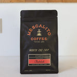 A black bag of Mescalito Coffee’s Single Origin Whole Coffee Beans | Chelchele sits on a light surface, labeled “Ethiopia Chelchele, Medium Roast,” crafted by anaerobic natural process with notes of peach, mango, basil, and honey.