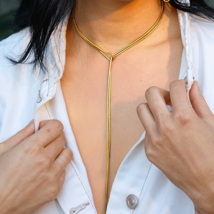 A person wearing a white shirt fastened at the bottom and an elegant gold Slipknot Necklace from Peter and June.