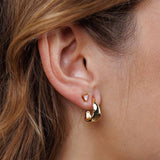 Close-up of a person's ear wearing Small Ripple Gold Hoop Earrings by JaxKelly—hypoallergenic, tarnish-free jewelry.